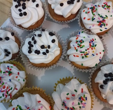 Cupcakes de vainilla recién horneados con glaseado de remolino blanco, chispas de chocolate y chispa