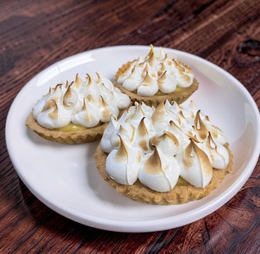 Tres tartas caseras de merengue de limón con picos tostados en un plato blanco sobre un fondo de mad