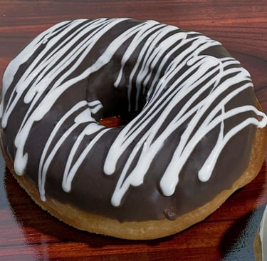 Donut glaseado de chocolate fresco con llovizna de glaseado blanco sobre un fondo de madera oscura.