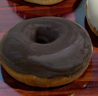 Donut glaseado de chocolate fresco con un suave glaseado oscuro sobre una mesa de madera.