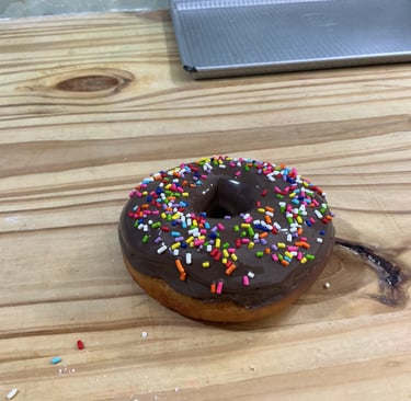 Donut glaseado de chocolate recién horneado con coloridas chispas de arco iris sobre una mesa de mad