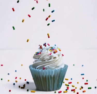 Cupcake de vainilla con glaseado blanco y coloridas chispas de arco iris cayendo sobre un fondo blan