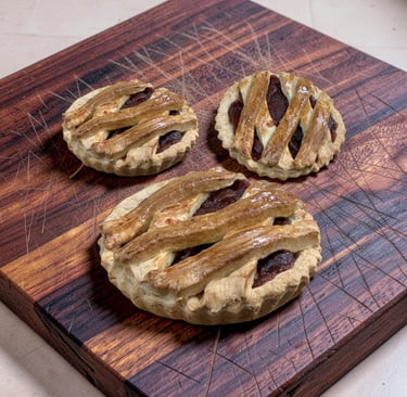 Tres mini tartas de frutas de celosía caseras enfriándose en una tabla de cortar de madera rústica.