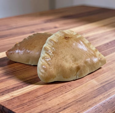 Dos empanadas caseras horneadas de color marrón dorado sentadas en una tabla de cortar de madera.