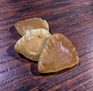 Tres mini empanadas de color marrón dorado o pasteles de mano sobre una mesa de madera oscura.