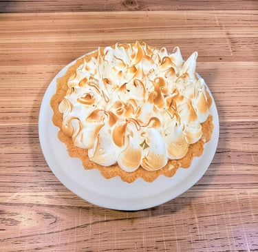 Una tarta casera de merengue de limón con picos tostados en un plato blanco sobre una mesa de madera