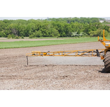 Agricultural field sprayer boom applying liquid fertilizer to tilled farm soil.
