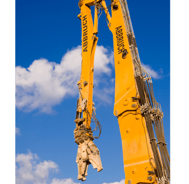Long-reach demolition excavator with a hydraulic concrete cutter attachment against a blue sky.