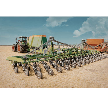 A modern green agricultural tractor pulling a large precision seed drill planter across a harvested field.