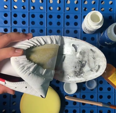Hand applying leather glue to a white sneaker sole for professional shoe repair and restoration.