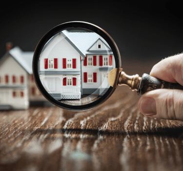 Hand holding a magnifying glass over a model house for real estate inspection and property search.