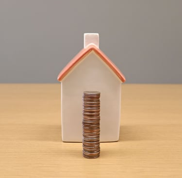 A stack of silver coins in front of a small ceramic house model representing real estate savings and mortgage payments.