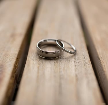 Elegant silver wedding bands, one plain and one diamond-studded, lie on rustic wooden planks, symbolizing marriage and