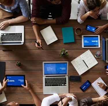 Overhead view of a business team collaborating at a wooden table with laptops and digital tablets.