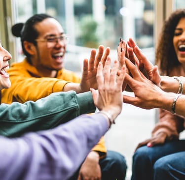 a group of people sitting around a table with their hands together