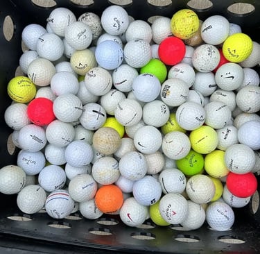 A black plastic crate overflowing with assorted used golf balls including Titleist, Callaway, and Srixon brands.