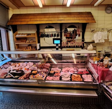 Metzgerei-Innenraum mit beleuchteten Auslagen, in denen verschiedene Fleischsorten und Wurstprodukte