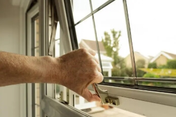 Hand opening a window latch on a residential window.
