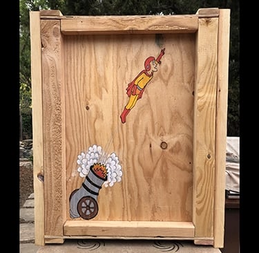 Shipping crate for Talbotics sculpture with image of human cannonball drawn on it.