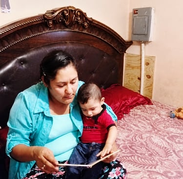 Mother reading a book with her toddler son while sitting on a bed.