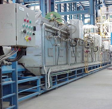 Conveyor oven machine with control panels in a manufacturing factory setting.