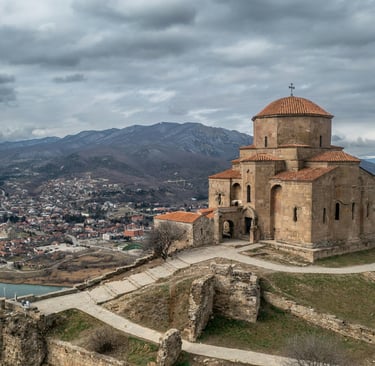 Ancient Jvari Monastery overlooking Mtskheta and the river confluence in Georgia under a cloudy sky.