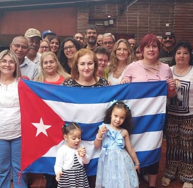 A diverse group of smiling people standing together and holding the national flag of Cuba at an outdoor event.