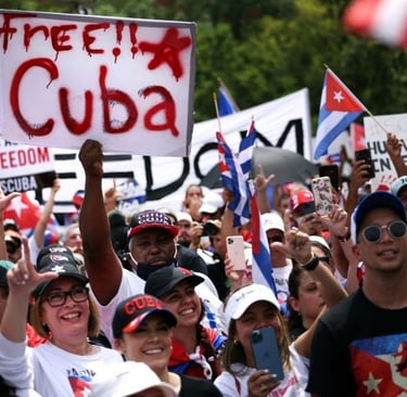 Protesters at a rally holding a Free Cuba sign and Cuban flags to support political freedom.