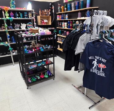 Gift shop interior with 3D printed dragons, colorful tumblers, and custom graphic t-shirts on display.