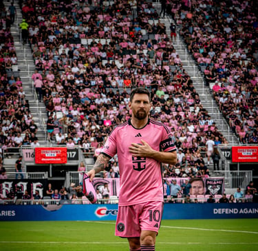 Lionel Messi in a pink Inter Miami jersey walking on the pitch in front of a crowded stadium.