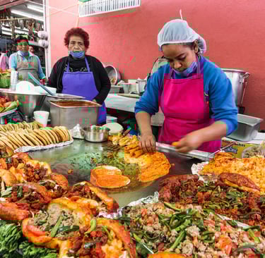 Street food vendors preparing authentic pambazos and tacos on a large griddle at a Mexican market.