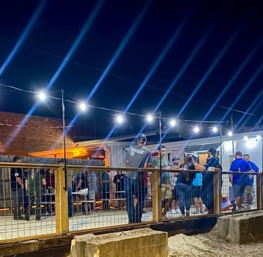 Crowd of people enjoying an outdoor nightlife event with string lights and blue stage beams.