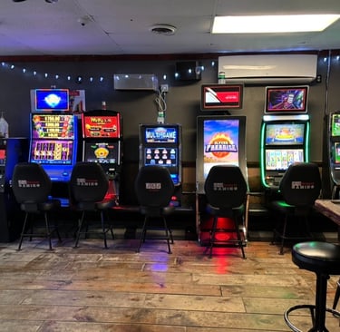 Video gaming terminal slot machines lined up inside a bar with wood floors and neon lights.