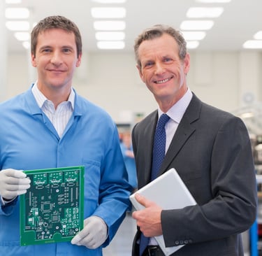 Engineer and business partner reviewing electronic circuit board in production facility.