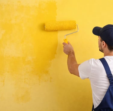 a man in overalls and a hat, painting a wall with a roller 