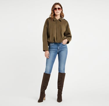 a woman in a green faux jacket, jeans and boots