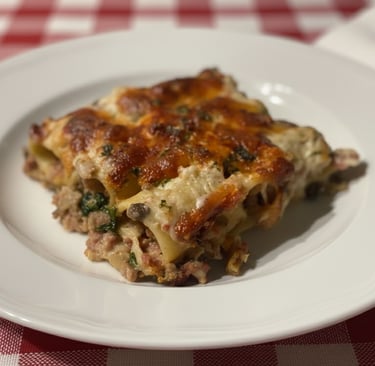 Baked cannelloni pasta with melted cheese and meat sauce on a white plate with a red checkered tablecloth.