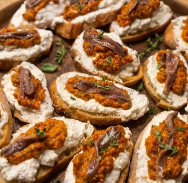 Gourmet bruschetta appetizers topped with ricotta cheese, red pesto, and anchovies on a wooden platter.