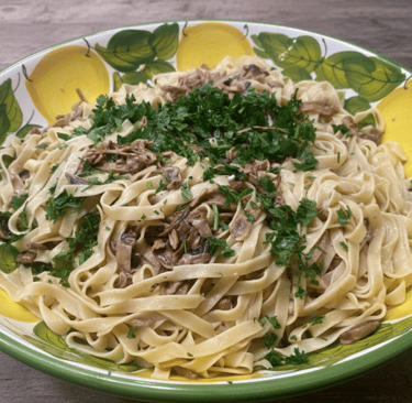 Creamy mushroom fettuccine pasta topped with fresh parsley in a ceramic lemon-patterned bowl.