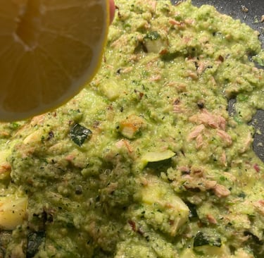 Fresh lemon juice being squeezed over a healthy green zucchini and tuna sauce cooking in a pan.
