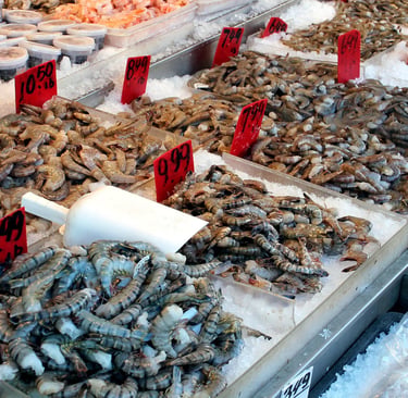 Fresh raw shrimp and prawns on ice at a seafood market display with red price tags.
