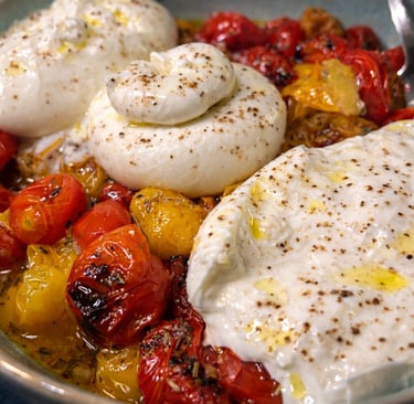 Fresh burrata cheese topped with black pepper and olive oil over roasted cherry tomatoes in a bowl.