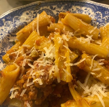 Rigatoni pasta with savory meat bolognese sauce and grated parmesan cheese on a blue floral plate.