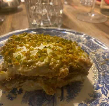 Slice of creamy pistachio tiramisu dessert topped with crushed nuts on a blue floral plate.
