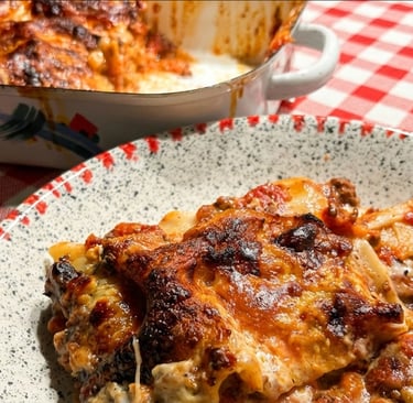 A serving of homemade meat lasagna with melted cheese on a speckled plate with a red checkered tablecloth.