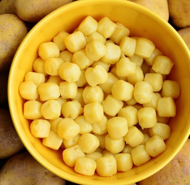Fresh homemade potato gnocchi served in a bright yellow bowl surrounded by raw whole potatoes.
