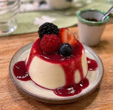 Creamy vanilla panna cotta dessert topped with berry coulis, fresh strawberries, and blackberries.