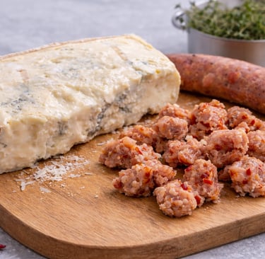 Gorgonzola cheese block with crumbled Italian salsiccia sausage on a wooden board.