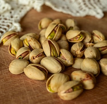 A pile of roasted, salted pistachios in their shells on a rustic wooden table with white lace.