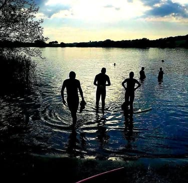 James Oswald Silhouetted swimmers preparing for open water swimming in a calm lake at sunset.